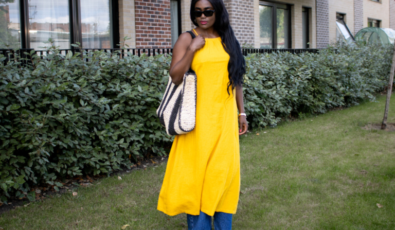 What to wear in Sub-Saharan Africa in July and August – woman in sunglasses wearing a yolk yellow linen dress over wide-leg blue jeans