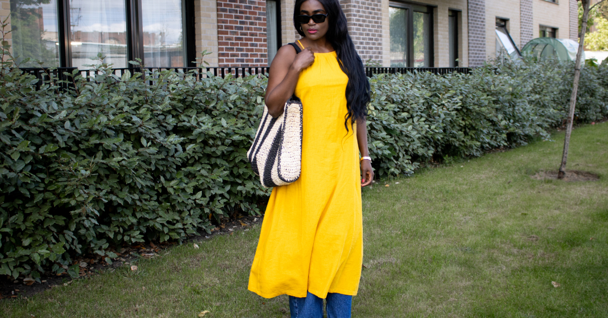 What to wear in Sub-Saharan Africa in July and August – woman in sunglasses wearing a yolk yellow linen dress over wide-leg blue jeans