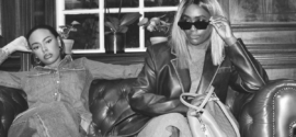 Two stylish women seated on a leather sofa, each showcasing distinct fashion personalities—one in double denim, the other in an oversized blazer and sunglasses.