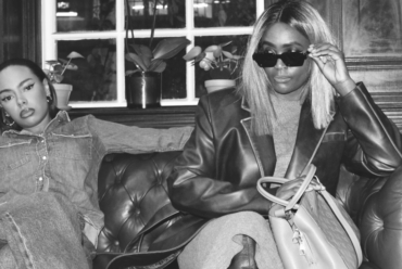Two stylish women seated on a leather sofa, each showcasing distinct fashion personalities—one in double denim, the other in an oversized blazer and sunglasses.