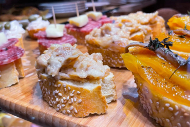 A diverse cicchetti platter on a rustic wooden board, showcasing various Venetian small tapas-like bites.