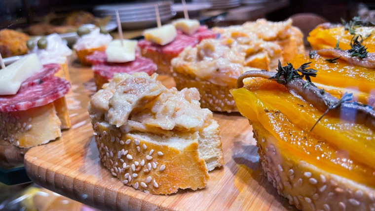 A diverse cicchetti platter on a rustic wooden board, showcasing various Venetian small tapas-like bites.