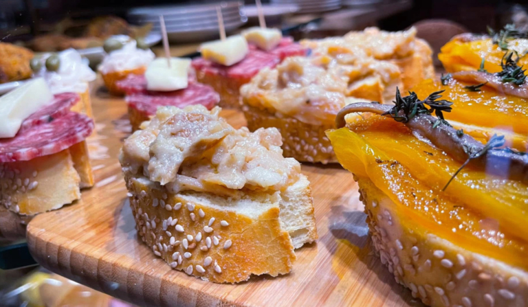 A diverse cicchetti platter on a rustic wooden board, showcasing various Venetian small tapas-like bites.