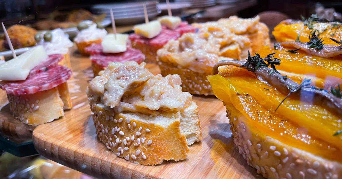 A diverse cicchetti platter on a rustic wooden board, showcasing various Venetian small tapas-like bites.