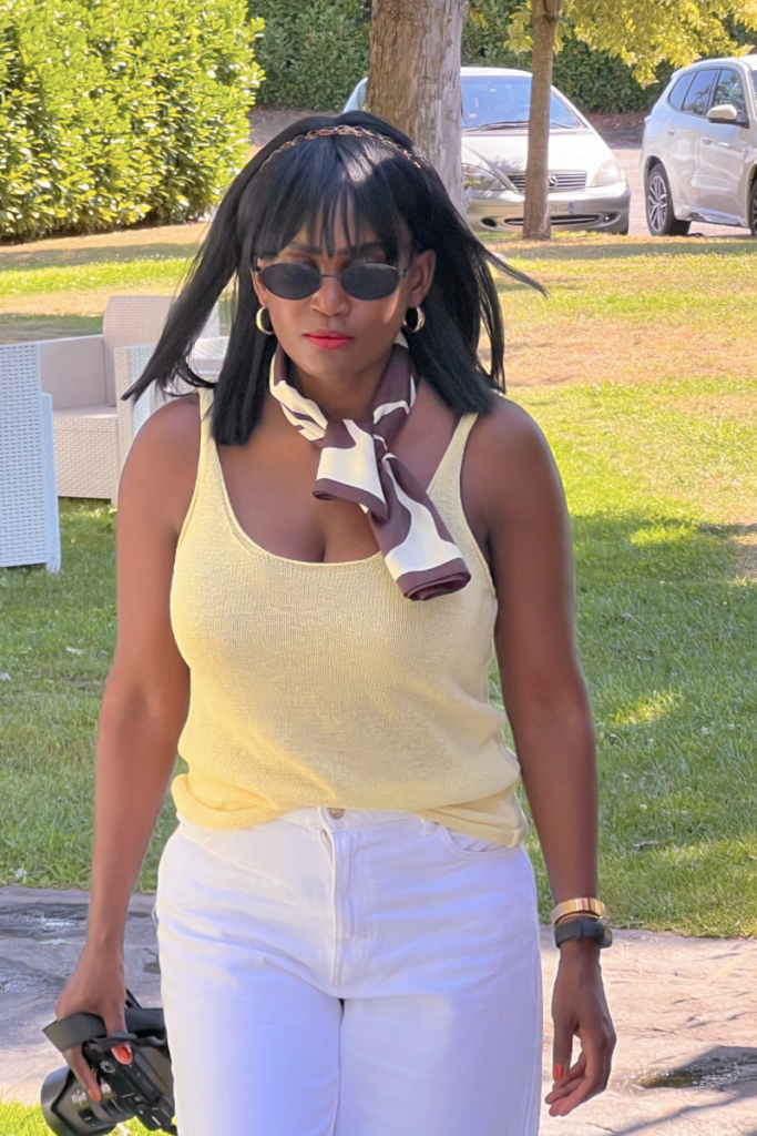 Woman outdoors in a sleeveless yellow top and white jeans, wearing sunglasses and a sleek French bob wig with fringe—showcasing one of the chicest bob wig styles for summer.