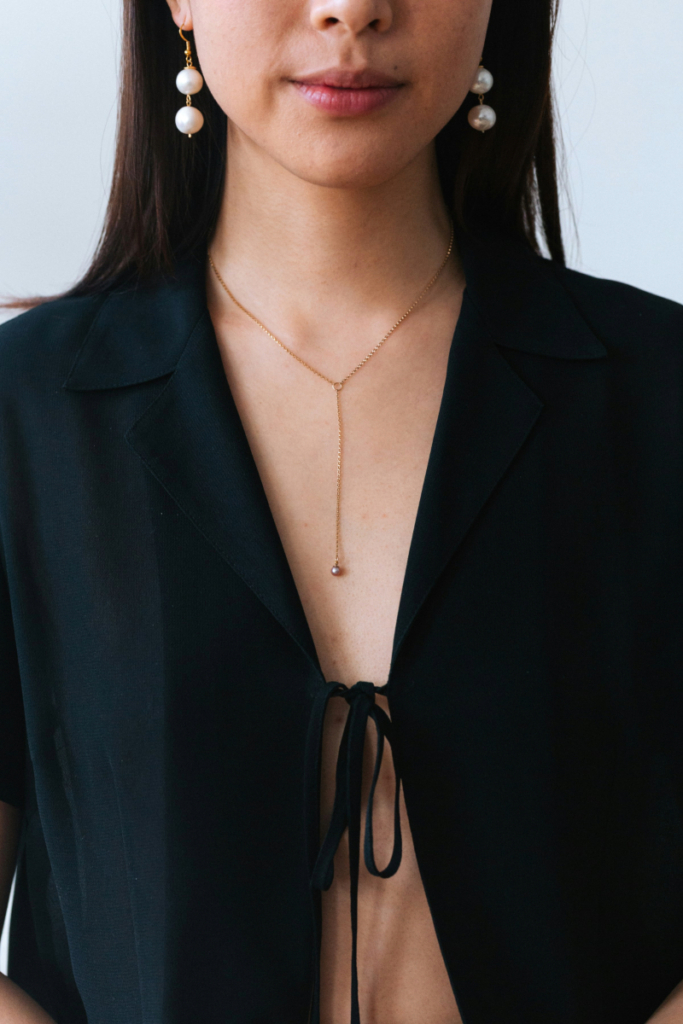 A woman wears an open V-neck top paired with a delicate thin lariat necklace, creating an elegant, minimalist look.