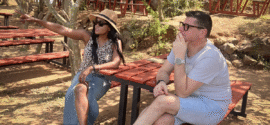 A woman sitting outdoors in sunglasses, pointing ahead while talking with a man, reflecting on her word of the year.