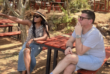 A woman sitting outdoors in sunglasses, pointing ahead while talking with a man, reflecting on her word of the year.