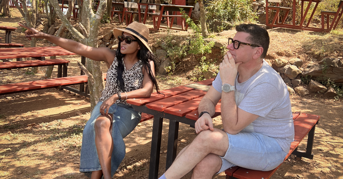A woman sitting outdoors in sunglasses, pointing ahead while talking with a man, reflecting on her word of the year.