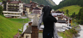 Woman in black outfit with patterned scarf overlooking the village of Sölden in the Austrian Alps on a rainy late-summer day