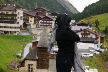 Woman in black outfit with patterned scarf overlooking the village of Sölden in the Austrian Alps on a rainy late-summer day