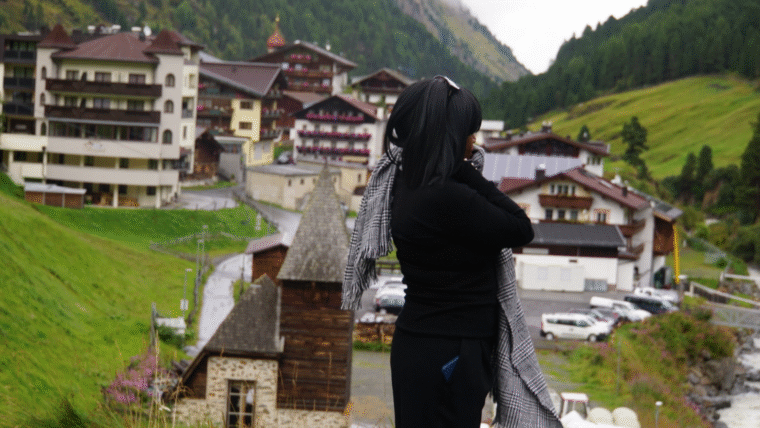 Woman in black outfit with patterned scarf overlooking the village of Sölden in the Austrian Alps on a rainy late-summer day