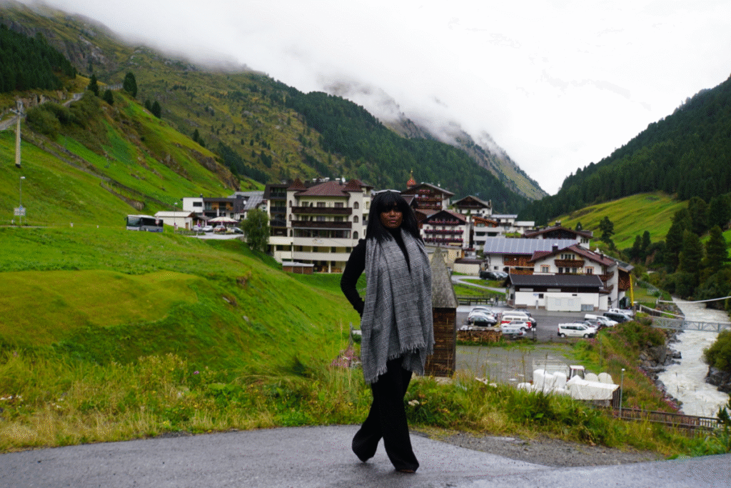 A person views the scenic Sölden village in late August, with misty green mountains and traditional buildings.
