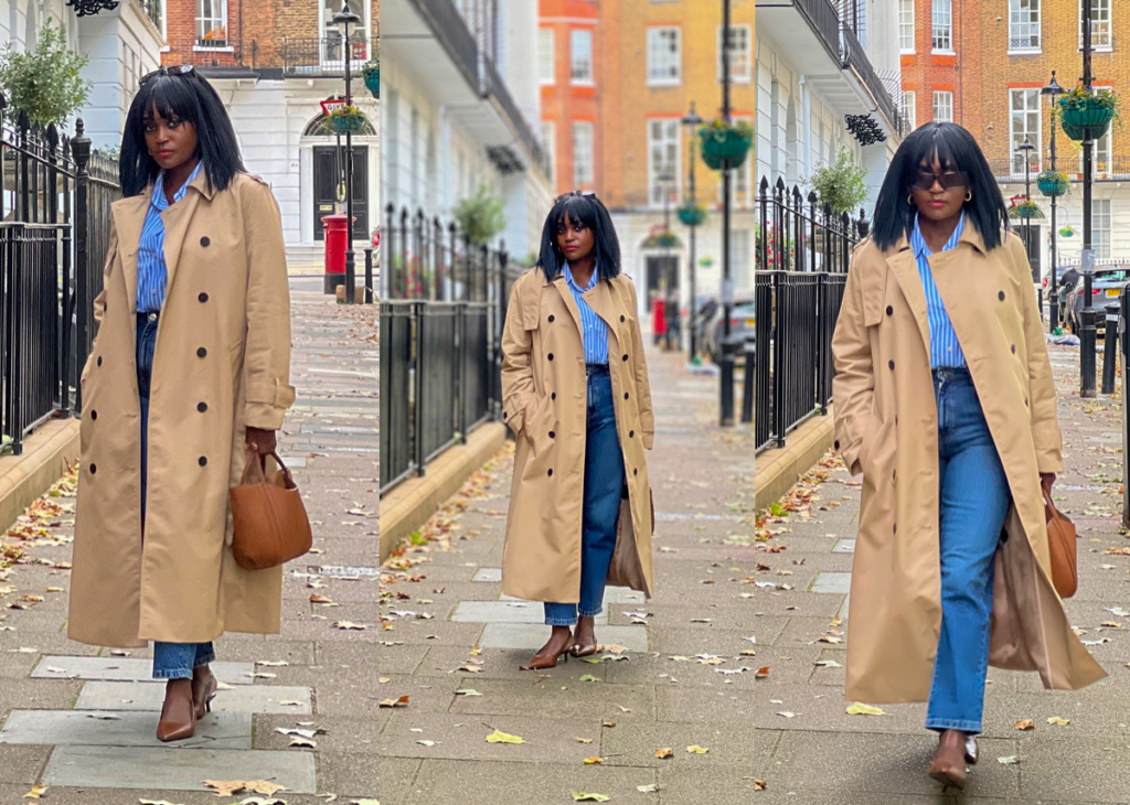 A woman wearing a flattering beige trench coat for autumn, styled with blue jeans, a striped shirt, and brown kitten heels on a London street.