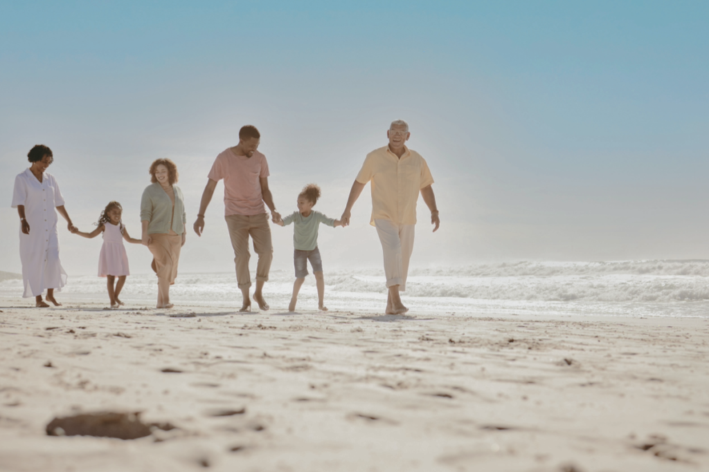 A multigenerational family walks together along a beach, with grandparents, parents, and children enjoying time by the sea.