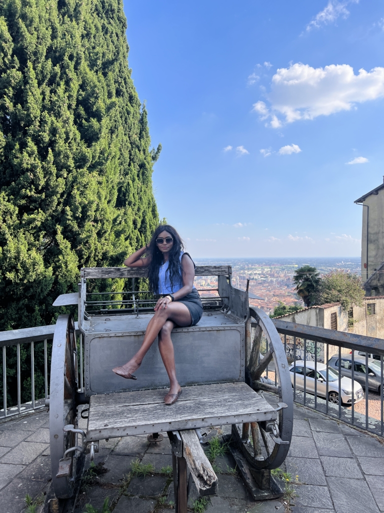 Woman seated on a historic wooden cart in Bergamo’s Città Alta overlooking the city of Bergamo, Italy.