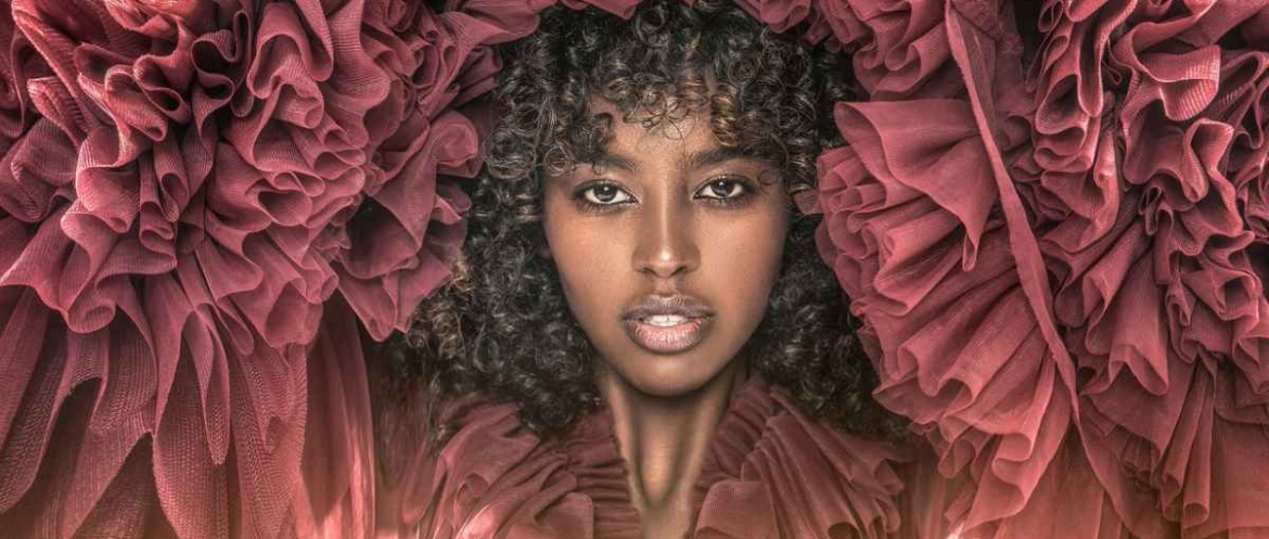 A Black woman with a natural curly afro wearing a layered maroon tulle dress, representing dressing for Valentine’s Day with confidence, ease and personal style.