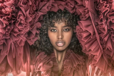 A Black woman with a natural curly afro wearing a layered maroon tulle dress, representing dressing for Valentine’s Day with confidence, ease and personal style.