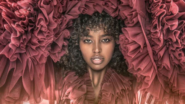 A Black woman with a natural curly afro wearing a layered maroon tulle dress, representing dressing for Valentine’s Day with confidence, ease and personal style.
