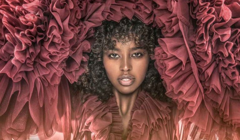 A Black woman with a natural curly afro wearing a layered maroon tulle dress, representing dressing for Valentine’s Day with confidence, ease and personal style.