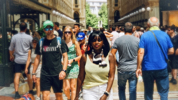 Woman walking through a busy Milan arcade surrounded by summer crowds, reflecting on the shift toward second city travel.