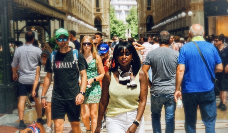 Woman walking through a busy Milan arcade surrounded by summer crowds, reflecting on the shift toward second city travel.
