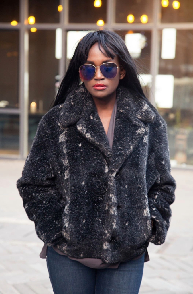 Woman wearing a faux fur coat and sunglasses on a street during a winter style slump, styled in layered winter neutrals.