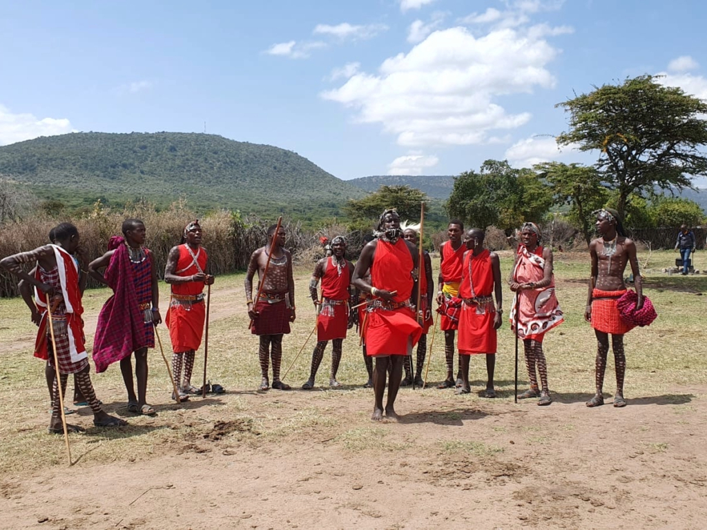 Maasai warriors in red traditional clothing performing a dance in a village in Kenya.