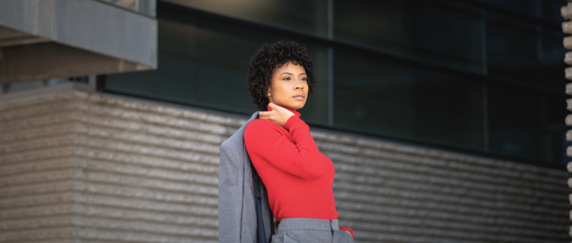 Woman wearing a red turtleneck sweater with a grey tailored suit standing outdoor.