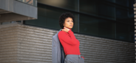 Woman wearing a red turtleneck sweater with a grey tailored suit standing outdoor.
