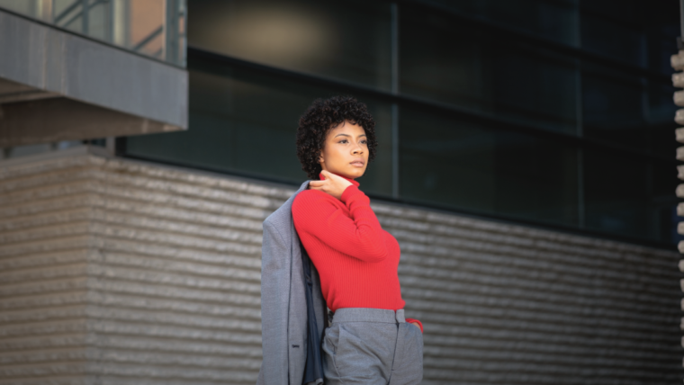 Woman wearing a red turtleneck sweater with a grey tailored suit standing outdoor.