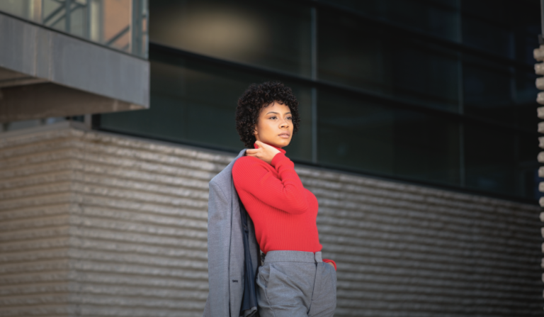 Woman wearing a red turtleneck sweater with a grey tailored suit standing outdoor.
