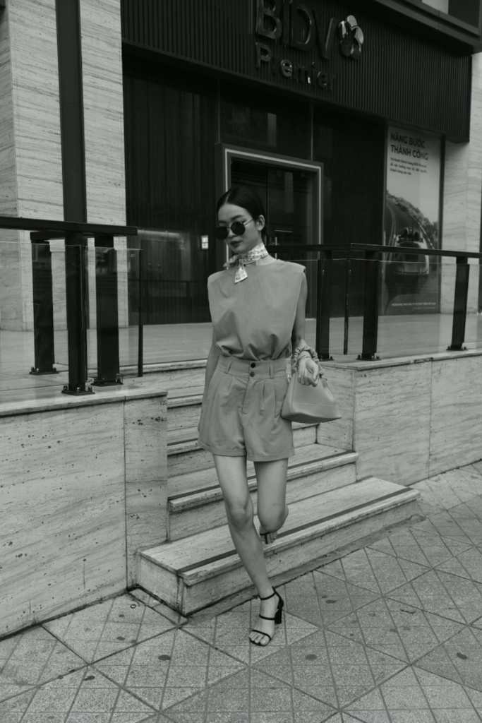 Woman wearing sunglasses, a scarf and tailored shorts standing outside a modern building