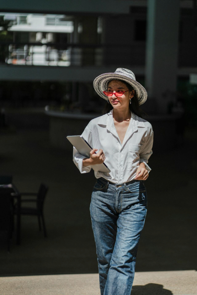 Woman wearing a white shirt, blue jeans, straw hat and red sunglasses walking indoors