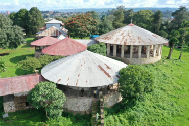 Aerial view of circular traditional buildings with metal roofs surrounded by lush greenery in an African town