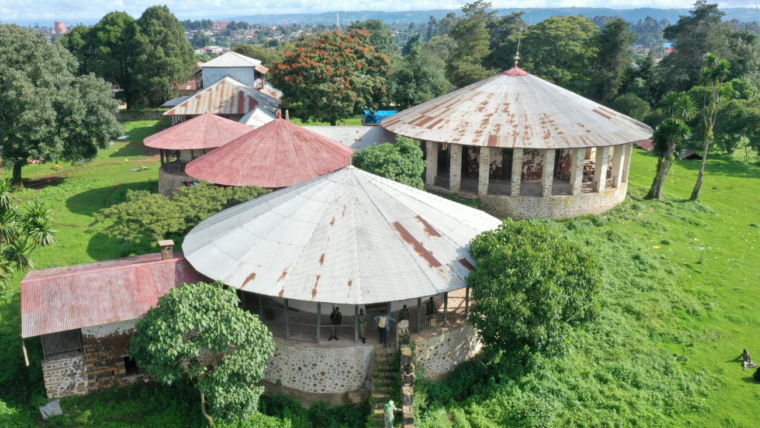 Aerial view of circular traditional buildings with metal roofs surrounded by lush greenery in an African town