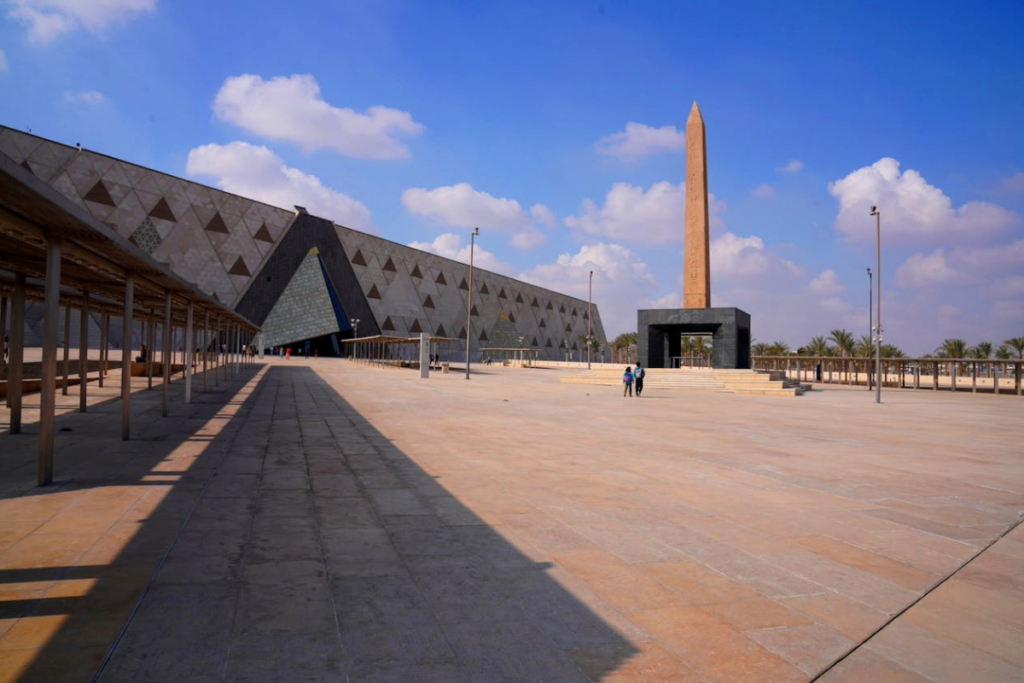 Exterior view of the Grand Egyptian Museum in Cairo with an obelisk monument and modern geometric building under a blue sky