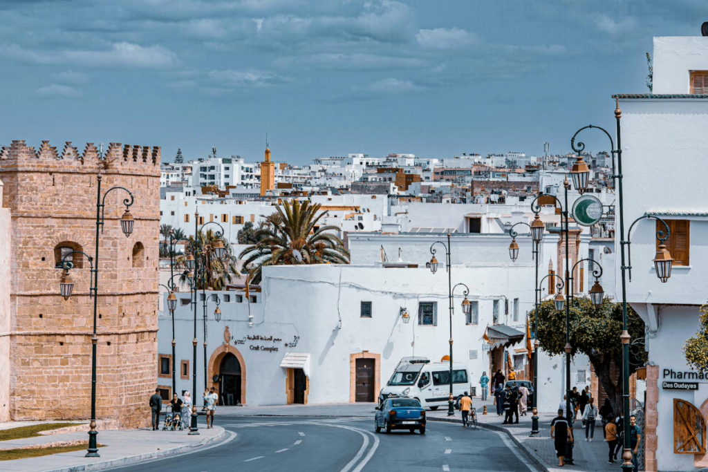 Street scene in Rabat Morocco with white buildings, historic tower, and people walking along a curved road