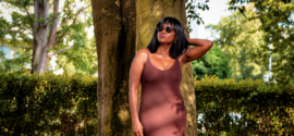 Woman in earthy brown sleeveless dress standing under a tree for shade, wondering what to wear in this heat.