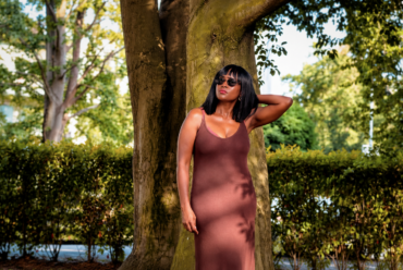 Woman in earthy brown sleeveless dress standing under a tree for shade, wondering what to wear in this heat.