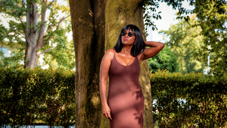 Woman in earthy brown sleeveless dress standing under a tree for shade, wondering what to wear in this heat.