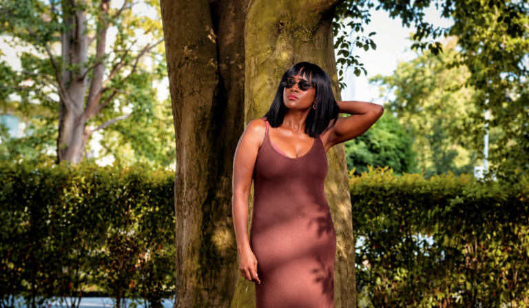 Woman in earthy brown sleeveless dress standing under a tree for shade, wondering what to wear in this heat.